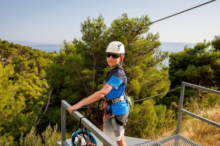 Photo for School boy preparing for zipline adventure. Happy active child put safety helmet on head. Summer fun with climbing in mountains - Royalty Free Image