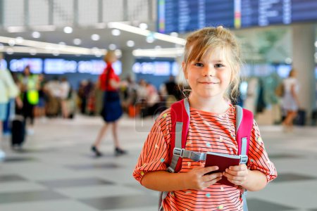 Foto de Una niña preescolar en la terminal del aeropuerto. Feliz niño que se va de vacaciones en avión. Niño sonriente con pasaporte y bolso - Imagen libre de derechos