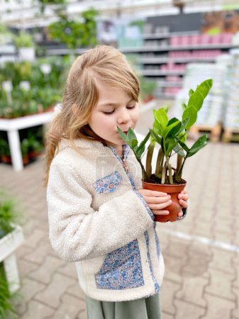 Photo for Cute girl holding potted plant in a flower shop. Little farmer choosing and buying green plants for home. Happy child - Royalty Free Image
