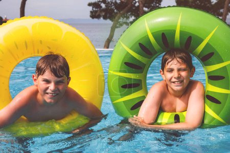 Téléchargez les photos : Deux enfants garçons s'amusent sur des anneaux gonflables en caoutchouc dans la piscine extérieure. Vacances d'été. Week-end d'été pour enfants. Enfants qui s'amusent, frères en vacances en famille - en image libre de droit