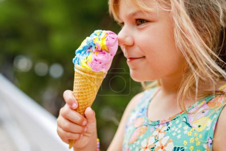 Photo for Happy preschool girl eating colorful ice cream in waffle cone on sunny summer day. Little toddler child eat icecream dessert. Sweet food on hot warm summertime days. Bright light, colorful ice-cream. - Royalty Free Image