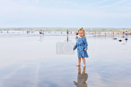 Photo for Little cute toddler girl at the Ballybunion surfer beach, having fun on with playing on west coast of Ireland. Happy child enjoying Irish summer and sunny day with family - Royalty Free Image