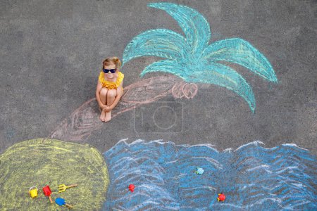 Photo for Happy little preschool girl in swimsuit with sea, sand, palm painted with colorful chalks on asphalt. Cute child with having fun with chalk picture. Summer, vacations, summertime. - Royalty Free Image