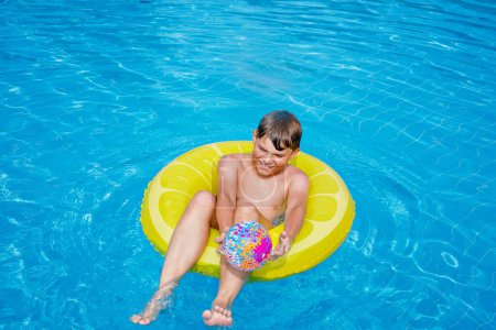 Photo for Cool school boy having fun on inflatable rubber circle in outdoor pool. Summer holiday. Summertime kids weekend. Child in swiming pool. Funny kid boy on ring at aquapark on family vacation - Royalty Free Image