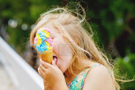 Photo for Happy preschool girl eating colorful ice cream in waffle cone on sunny summer day. Little toddler child eat icecream dessert. Sweet food on hot warm summertime days. Bright light, colorful ice-cream. - Royalty Free Image