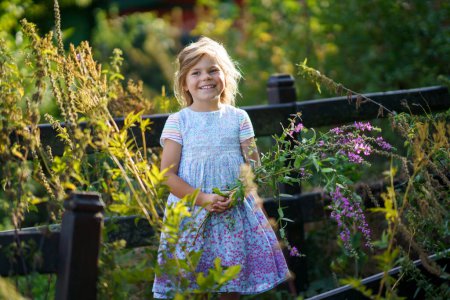 Foto de Retrato de una linda niña preescolar con flores silvestres al aire libre. Feliz niño divertido en la soleada noche de verano. - Imagen libre de derechos