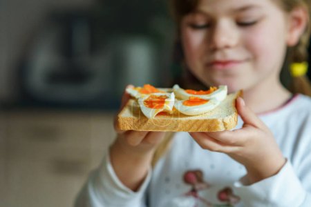 Photo for Little smiling girl have a breakfast at home. Preschool child eating sandwich with boiled eggs. Happy children, healthy food and meal - Royalty Free Image