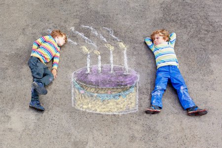 Téléchargez les photos : Deux petits enfants heureux s'amusent avec grand dessin d'image de gâteau d'anniversaire avec des craies colorées. Loisirs créatifs pour les enfants à l'extérieur en été. Enfants soufflant des bougies
. - en image libre de droit