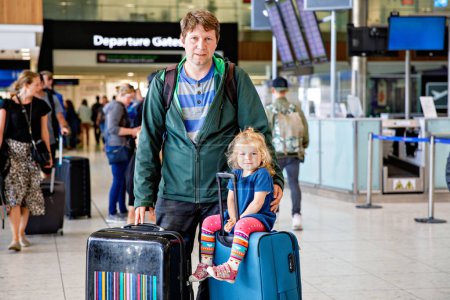 Photo for Cute little toddler girl and father at the airport. Happy family traveling by plane, making vacations. Young dad and baby daughter with suitcases waiting for flight. Family going on journey. Ireland. - Royalty Free Image