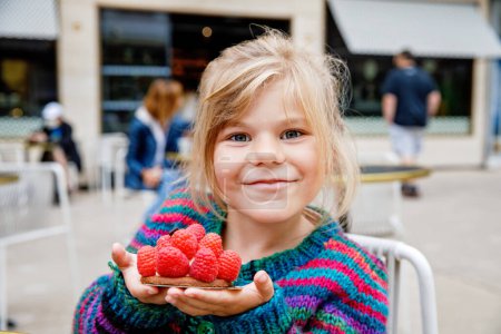 Photo for Adorable little girl and delicious raspberry cake. Preschool child eating sweet dessert in French outdoor cafe - Royalty Free Image