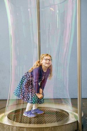 Photo for Little preschool girl standing inside a huge soap bubble. Happy girl having fun - Royalty Free Image