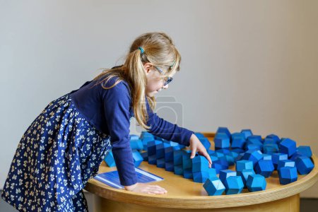 Photo for Little preschool girl playing with large blue logical objects cubes in children museum. Happy concentrated child with glasses thinking. Education and development concept. - Royalty Free Image