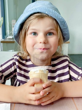 Photo for Beautiful little girl eats ice-cream in the summer. Happy funny preschool girl with sweet ice cream cone in the city - Royalty Free Image