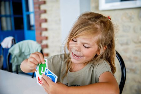 Photo for Excited smiling cute preschool girl playing card game. Happy healthy child plays with family. Creative indoors leisure and education of kid. Family activity at home - Royalty Free Image