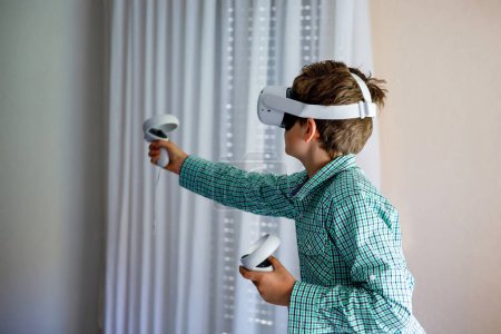 Photo for Young kid boy play VR games in virtual reality helmets at home. Exceted preteen child hold controllers and look away. Teenager in VR helmets playing video games - Royalty Free Image