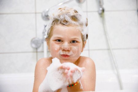 Photo for Cute child with shampoo foam and bubbles on hair taking bath. Portrait of happy smiling preschool girl health care and hygiene concept. Washes hair by herself - Royalty Free Image