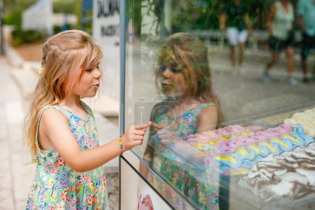Photo for Happy preschool girl choosing and buying ice cream in outdoor stand cafe. Cute child looking at different sorts of icecream. Sweet summer dessert on family vacations. Summertime - Royalty Free Image