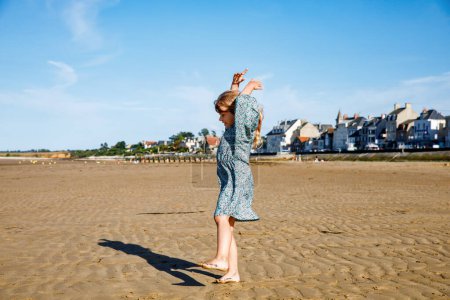 Téléchargez les photos : Preschool Girl joue sur une plage normande en Normandie, embrassant la joie des rivages sablonneux, des coquillages et de l'exploration sans soucis. Joyeuses vacances en famille et enfants en France - en image libre de droit