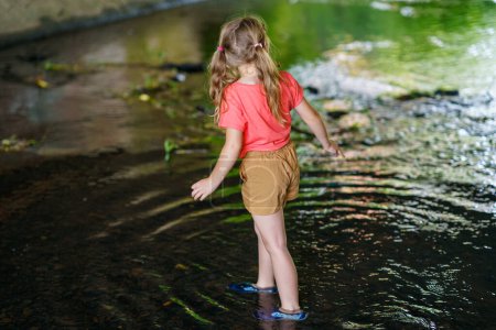 Téléchargez les photos : Une fille heureuse embrasse les joies de l'enfance alors qu'elle explore un ruisseau estival, s'immergeant dans des merveilles naturelles et des découvertes ludiques. Enfant d'âge préscolaire et été - en image libre de droit