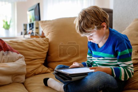 Téléchargez les photos : Écolier avec tablette. Étude d'écolier en ligne. Dispositif électronique pour apprendre, étudier et jouer à la maison. Petit garçon avec ordinateur portable PC. Gadget et temps d'écran pour les enfants. Enfant à la maison - en image libre de droit