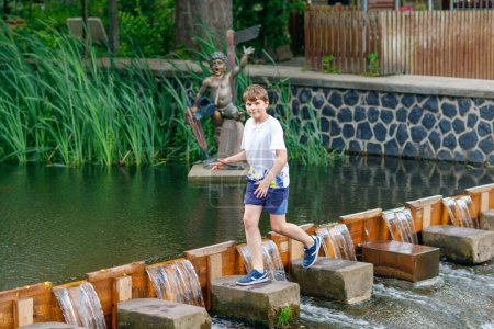 Téléchargez les photos : Enfant d'âge préscolaire s'amusant près d'une rivière par une journée d'été chaude et ensoleillée. Heureux enfant excité courir sur les pierres - en image libre de droit
