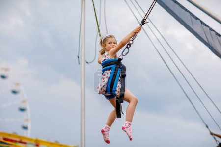 Téléchargez les photos : Petite fille d'âge préscolaire qui aime sauter avec une corde à sauter trampoline. Joyeux enfant dans le parc d'attractions. Activité familiale. - en image libre de droit