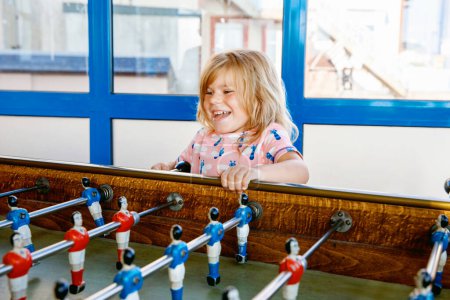 Photo for Little preschool girl playing table soccer. Happy excited positive child having fun with family game with siblings or friends - Royalty Free Image