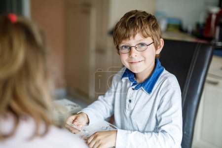 Téléchargez les photos : Petit garçon d'école actif avec des lunettes jouant au jeu de cartes avec sa copine à la maison. Loisirs créatifs et amusants pour les enfants du primaire. Meilleurs amis à l'école - en image libre de droit