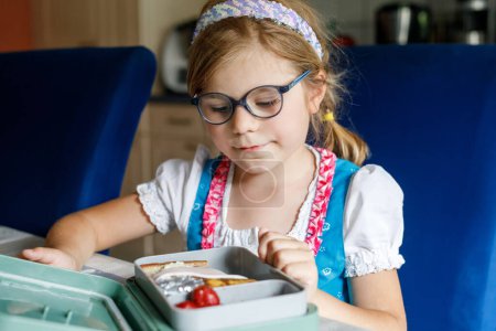 Photo for Cute Little Girl with Eyeglasses Eating Sandwich and Fruits during Break between Classes. Healthy Unhealthy Food for Kid. Breakfast Lunch Box for Children at School - Royalty Free Image