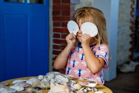 Photo for Little preschool girl with variation of different shells and clams at home. Happy child with collected shell from Normandy, France. Children, education, vacation concept - Royalty Free Image