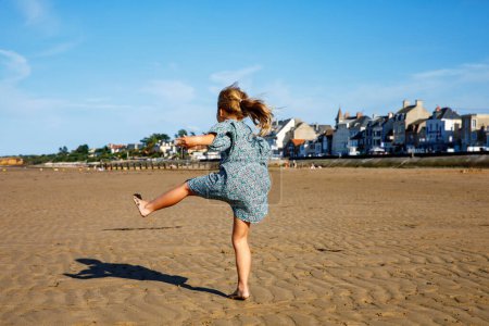 Téléchargez les photos : Preschool Girl joue sur une plage normande en Normandie, embrassant la joie des rivages sablonneux, des coquillages et de l'exploration sans soucis. Joyeuses vacances en famille et enfants en France - en image libre de droit