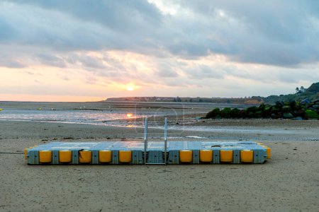 Téléchargez les photos : Vue du lever du soleil sur la rue côtière de Grandcamp Maisy, une ville côtière française pittoresque en Normandie, avec port de pêche, plages de sable fin et traditions maritimes - en image libre de droit
