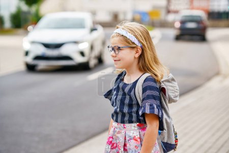 Foto de Niña preescolar en camino a la escuela. Healthy Happy Child Walking to Nursery School and Kindergarten. Niño sonriente con gafas y mochila en la calle City, al aire libre. Volver a la escuela - Imagen libre de derechos