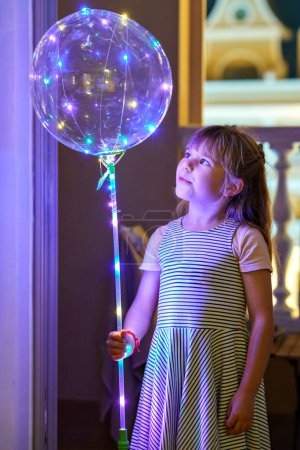 Foto de Niña con globo iluminado en la noche. Emocionado niño preescolar mirando las luces dentro del globo - Imagen libre de derechos
