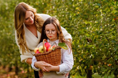 Photo for Happy school girl and beautiful mother with red apples in organic orchard. Happy woman and kid daughter picking ripe fruits from trees and having fun in garden. Harvest season for family - Royalty Free Image