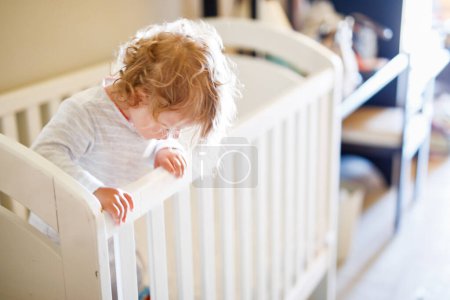 Photo for Cute Little Baby Girl Lying in Cot after Sleeping. Healthy Happy Child in Bed Climbing Out. Danger for Babies and Children - Royalty Free Image