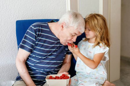 Photo for Grandpa And Granddaughter Eating Raspberries At Home. Happy Preschool Girl And Senior Man Having Fun Together. Child And Grandfather, Family Time - Royalty Free Image