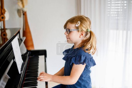 Téléchargez les photos : Belle petite fille de maternelle jouant du piano à l'école de musique. Enfant mignon s'amuser avec apprendre à jouer de l'instrument de musique. Éducation musicale précoce pour les enfants. - en image libre de droit