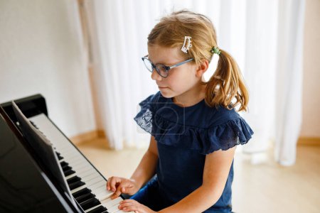 Photo for Beautiful little preschool girl playing piano at music school. Cute child having fun with learning to play music instrument. Early musical education for children. - Royalty Free Image