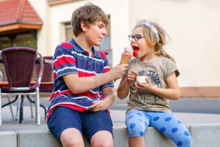 Photo for Little preschool girl and school kid boy eating ice cream in waffle cone Happy children, brother and sister eat icecream dessert. Family in the city. Siblings in love - Royalty Free Image
