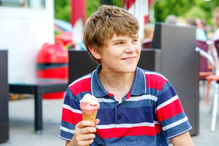 Photo for Cheerful laughing preteen boy eating multicolored ice cream in a waffle cone. Cool in the summer heat.Sweet snack for children. Happy child - Royalty Free Image