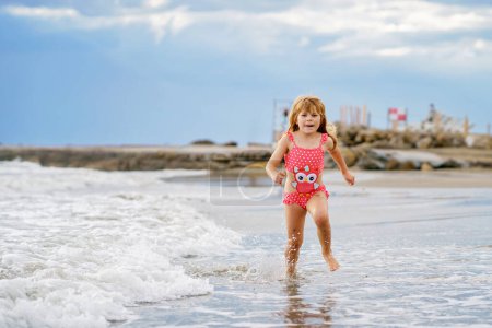 Foto de Niño feliz, niña preescolar en traje de baño corriendo y saltando en las olas durante las vacaciones de verano en la playa tropical exótica. Viaje familiar en la costa del océano - Imagen libre de derechos