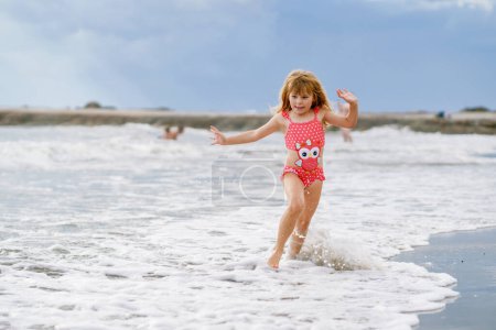 Foto de Niño feliz, niña preescolar en traje de baño corriendo y saltando en las olas durante las vacaciones de verano en la playa tropical exótica. Viaje familiar en la costa del océano - Imagen libre de derechos