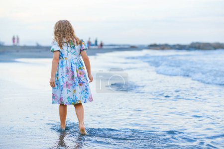 Photo for Happy Child, Little Preschool Girl in Dress Running And Jumping In The Waves During Summer Vacation On Exotic Tropical Beach by Sunset. Family Journey On Ocean Coast - Royalty Free Image
