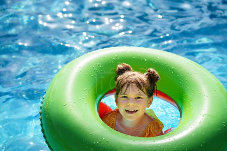 Foto de Niña feliz con anillo de juguete inflable flotar en la piscina. Pequeño niño preescolar aprendiendo a nadar y bucear en la piscina al aire libre del complejo hotelero. Actividad deportiva saludable y diversión para niños - Imagen libre de derechos
