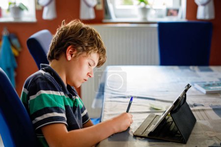 Photo for Preteen kid boy learning at home on laptop for school. School child making homework and using notebook and modern gadgets. Home schooling concept - Royalty Free Image