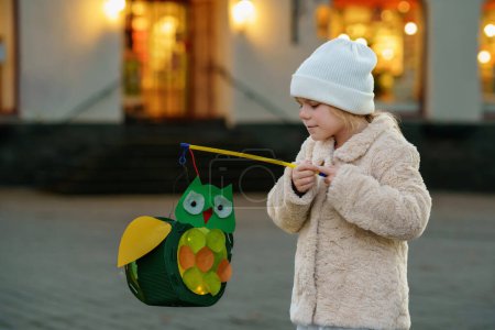 Photo for Little preschool kid girl holding selfmade traditional owl lanterns with candle for St. Martin procession. child happy about children and family parade in kindergarten. German tradition Martinsumzug. - Royalty Free Image