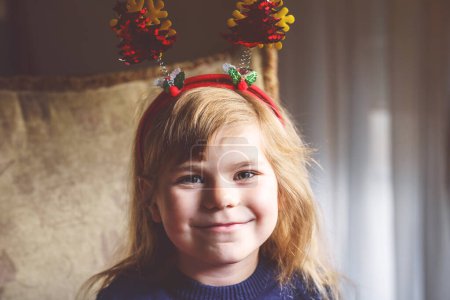 Téléchargez les photos : Portrait de petite fille d'âge préscolaire avec bandeau de sapin de Noël sur hed. Joyeux enfant souriant - en image libre de droit