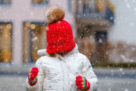 Téléchargez les photos : Drôle de portrait de petite fille d'âge préscolaire en vêtements d'hiver. Joyeux enfant positif avec chapeau rouge et gants colorés à l'extérieur. Jour d'hiver - en image libre de droit