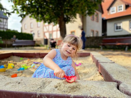Foto de Adorable niña en el patio de recreo en la arena. Niño jugando con moldes de arena y haciendo mudpies. Actividades creativas al aire libre para niños - Imagen libre de derechos